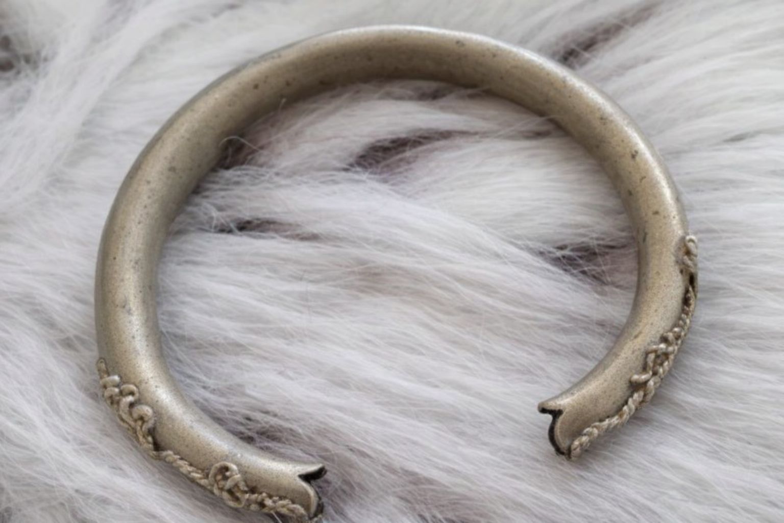 Ett antikt silverarmband vilandes på vit pälsbakgrund.