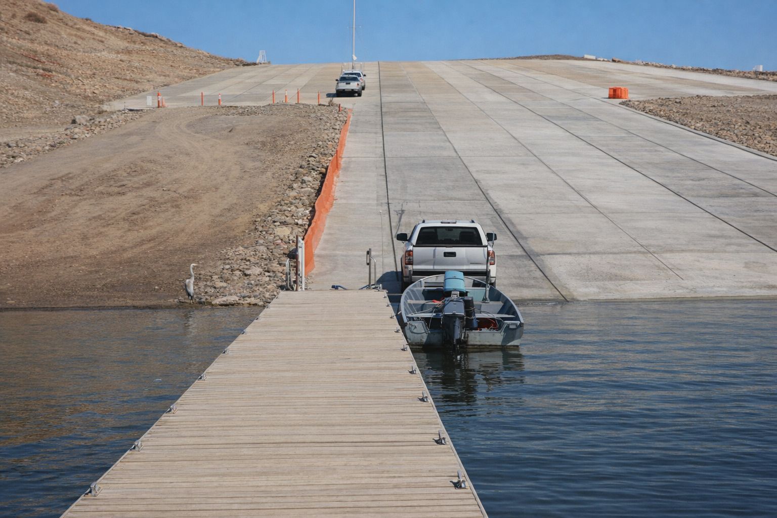 En vit pickupbil sjösätter en mindre båt vid en bred båtramp i skärgården.