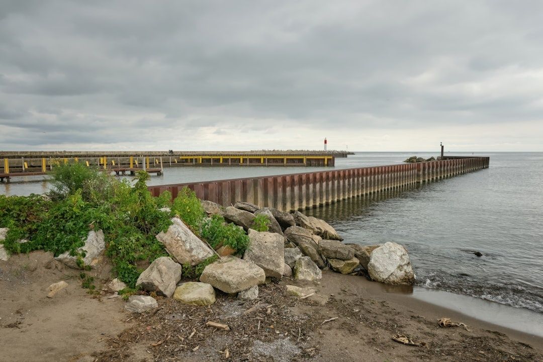 Stenig strand med lång vågbrytare och bryggor under molnig himmel
