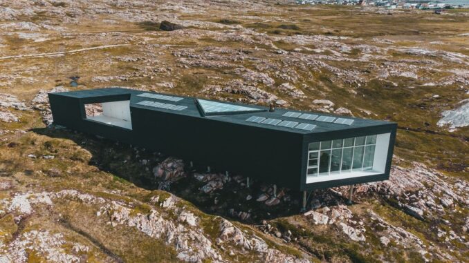 Modern svart byggnad med solpaneler på en karg, stenig ö