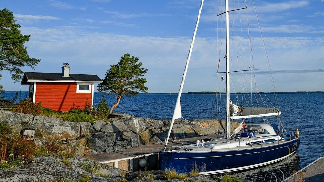 Segelbåt förtöjd vid en klippig skärgårdsbrygga intill röd stuga